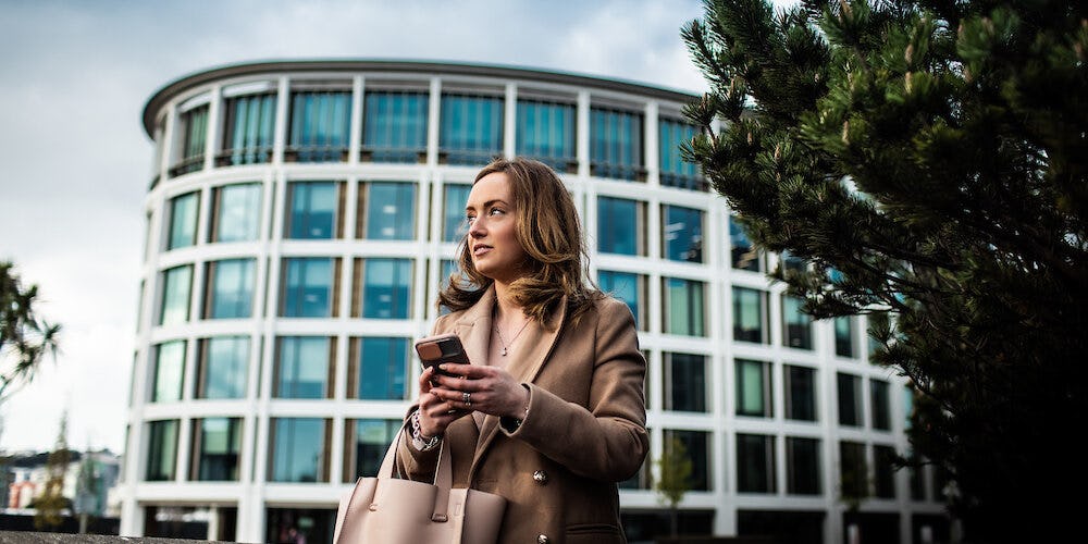 A woman holding a mobile phone stands in front of a financial services building