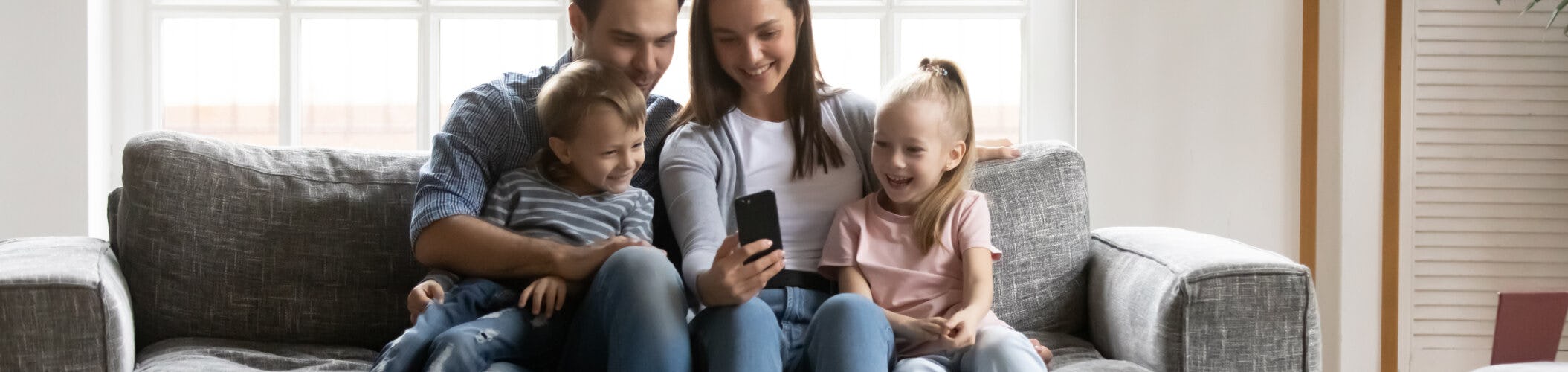 A man, woman and young children sit on a sofa looking at a mobile phone