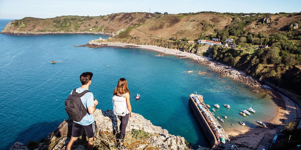 Two tourists stand on a cliffpath overlooking the north coast of Jersey